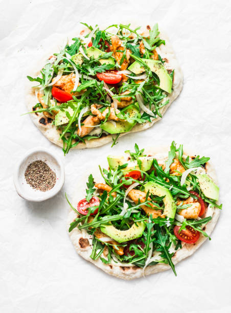 Pan-fried flatbread chicken, avocado, tomatoes, arugula pizza on a light background, top view