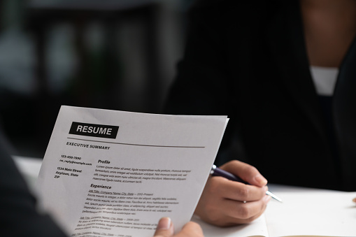 Human resources department manager reads CV resume document of an employee candidate at interview room. Job application, recruit and labor hiring concept.