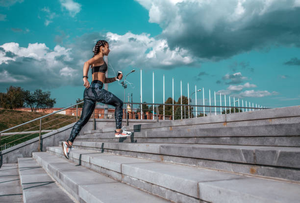 Young athletic girl running morning for jog, fitness training, sportswear, leggings and top. Phone listens music headphones. Summer city workout, online playlist application to Internet. Free space. stock photo