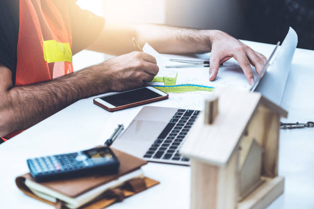 istock Young man construction worker or engineer working at desk with designer equipment to make interior design at workplace. Real estate business and civil engineering concept. 1134709774