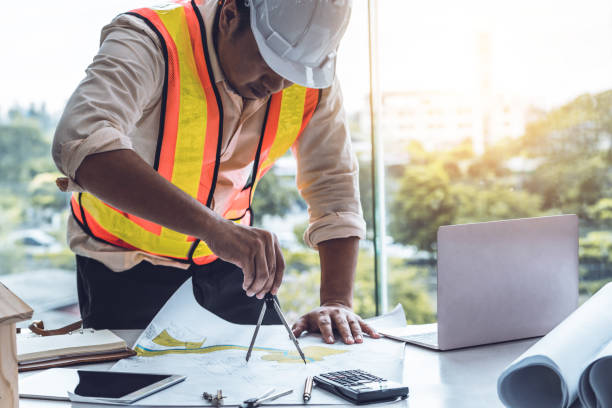 istock Young man architect or engineer working at desk with designer equipment to make interior design at workplace. Real estate business and civil engineering concept. 1134709788
