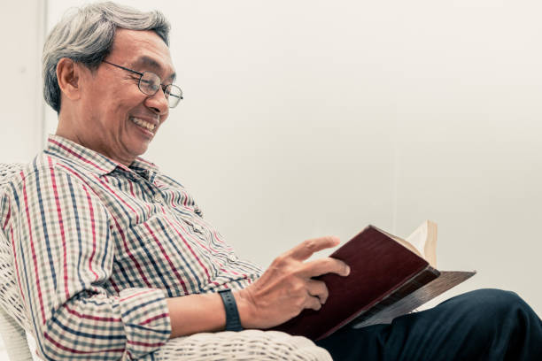 家庭でのリビングルームで椅子に本を読んで幸せなシニアアジアの男。退職生活・高齢化社会構想 - senior adult relaxation sofa reading ストックフォトと画像