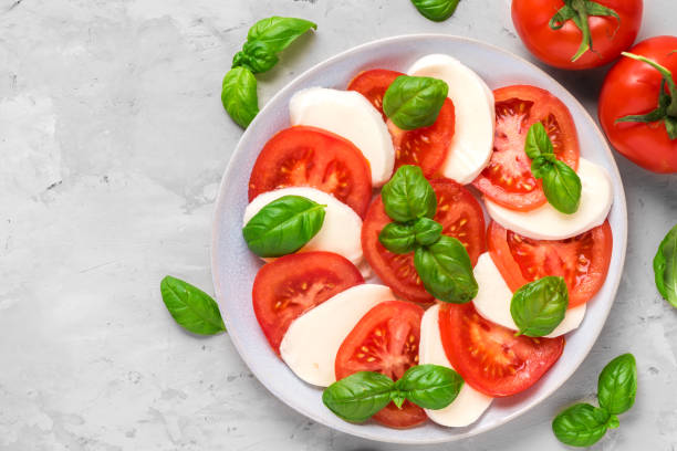 kapressalat mit reifen tomaten und mozzarella-käse, frische basilikumblätter auf beton. italienische küche - caprese salad fotos stock-fotos und bilder