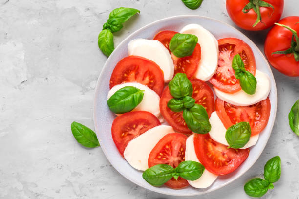 insalata caprese con pomodori maturi e mozzarella, foglie di basilico fresco su sfondo concreto. cibo italiano - salad food caprese salad gourmet foto e immagini stock