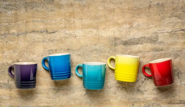 row of colorful stoneware coffee cups against textured handmade bark paper with a copy space