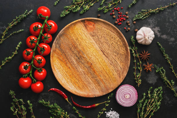 istock Flat lay empty wooden plate, vegetables, spices and herbs on dark stone background. Tomatoes, thyme, garlic, peppercorn, red onion, chili pepper, star anise. Top view 1134739083