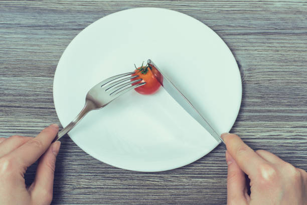 istock Concept of strict dieting. Woman's hands cutting little cherry tomato on empty plate 1134741586