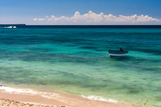 View of quiet beach without waves in Bahia de las Águilas, Dominican Republic where you can see a boat moored some clouds over a blue sky. The sea has a greenish-blue color