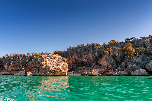 photograph of the cliffs of Bahia de las Aguilas in the Dominican Republic, the blue sea and the sky merge being separated by the line of light colored stones stained dark brown. There are few clouds in the sky.