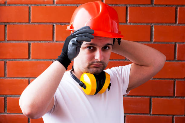istock A man in a protective helmet and black gloves against a red brick wall, with noise-reducing headphones around his neck. DIY concept and safety. 1134747909