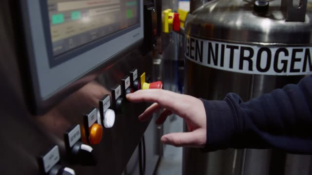 Caucasian Person Pushes a Button Next to a Tank of Liquid Nitrogen in an Indoor Manufacturing Facility