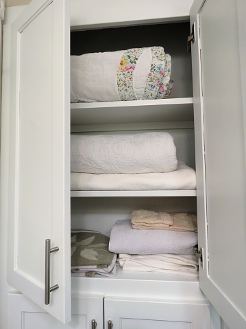 linen cabinet open in bathroom, shows towels, bedding