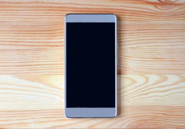istock Top view of a black empty screen smartphone isolated on light brown wooden table 1134753379