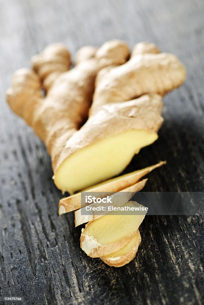 A piece of a ginger root that was sliced on partway Close up of sliced fresh ginger root spice on wooden table Chopped Food Stock Photo