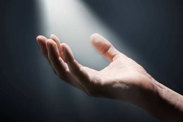 Bright light rays shihing on man's hand in darkness.