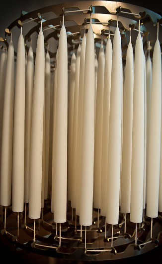 Many white wax candles hanging in bulk candlewicks to dry in a commercial candle-making production factory - Tools and process of making a traditional candle.