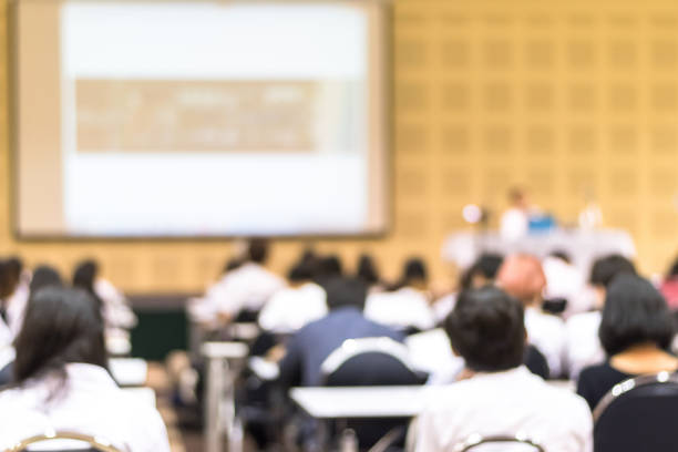 Speaker giving educational seminar, school lecture, or entrepreneurship business talk  blur background in conference meeting  with audiences or students in back of the room