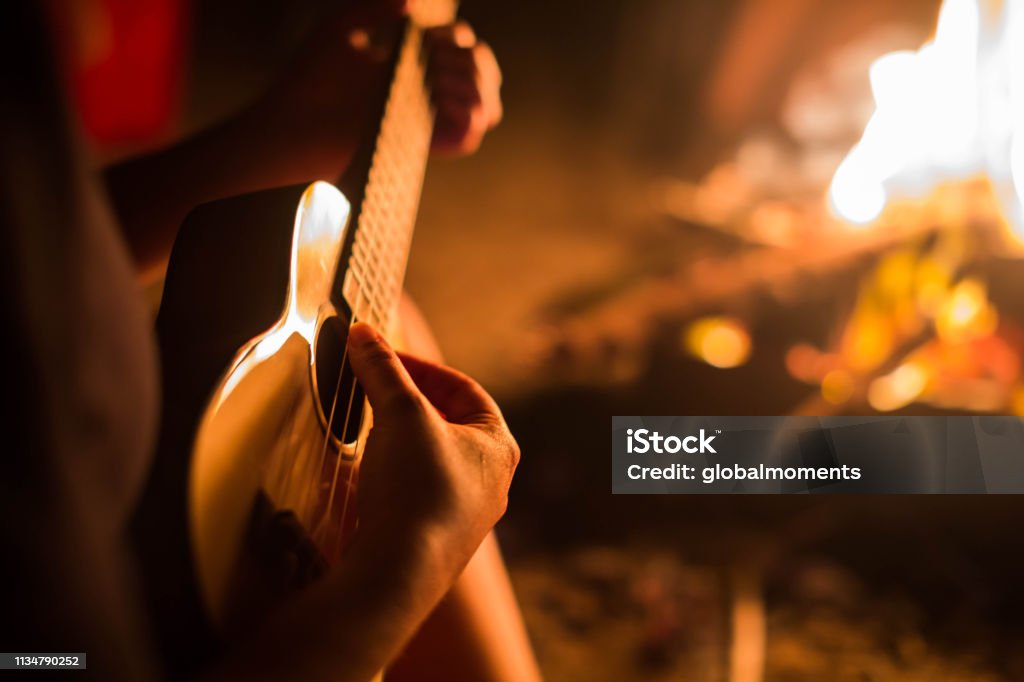 A Female Musician Playing Guitar Outside Sitting To A Fire Stock Photo - Download Image -