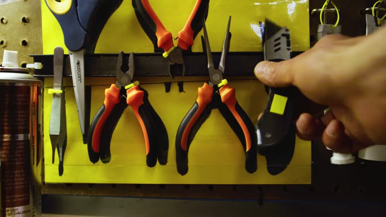 A Caucasian Man's Hand Replaces Needle-Nosed Pliers from a Magnetic Tool Holder and Picks Up a Box Knife in a Workshop