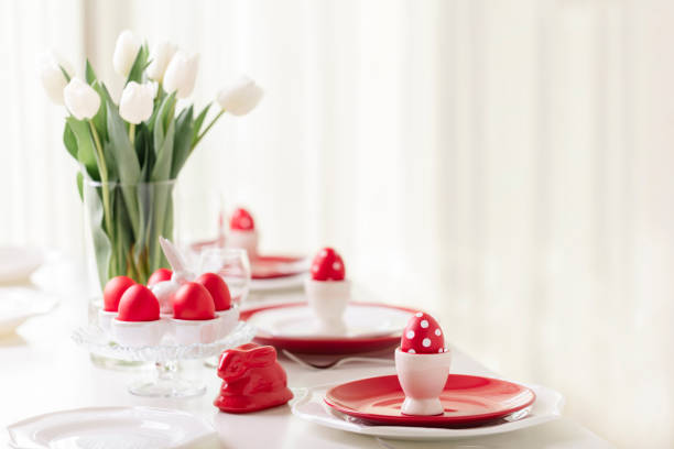 istock Happy easter. Decor and table setting of the Easter table is a vase with white tulips and dishes of red and white color. Easter colored eggs with white polka dots. 1134807325