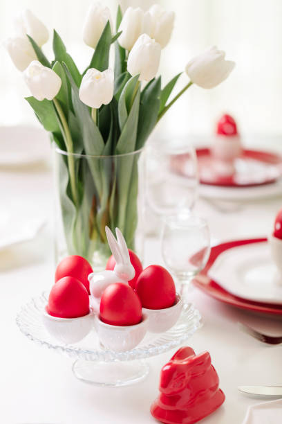 istock Happy easter. Decor and table setting of the Easter table is a vase with white tulips and dishes of red and white color. Easter colored eggs with white polka dots. 1134807331