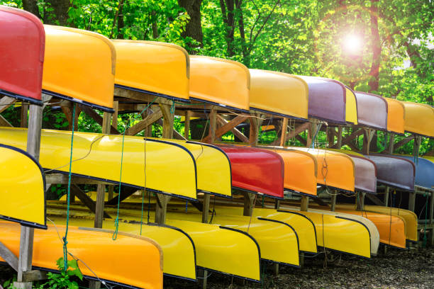 Lot of multi colored kayaks on the bank of the river, in summer or spring time. Colorful canoes or kayaking boats parked in the embarkation resort park. Sport, summer activity or teamwork concept. stock photo