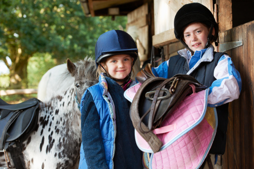 Two girls holding saddles with pony