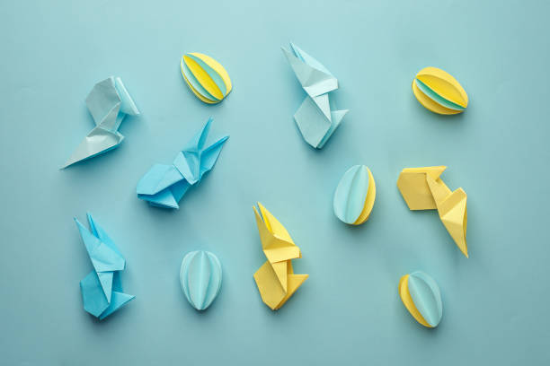 istock Creative Top view flat lay holiday composition Easter eggs funny bunny on blue paper background, copy space. Origami papercraft Easter day seasonal pattern 1134818229