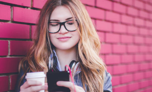 femme restant à côté du mur de brique avec le café préféré et utilisant le téléphone mobile. - red text messaging cafe teenage girls photos et images de collection