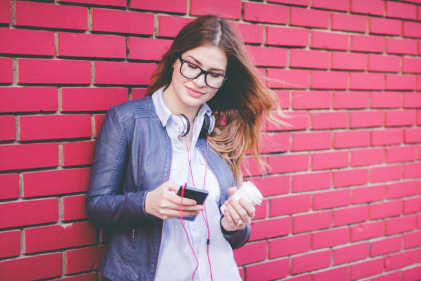 femme restant à côté du mur de brique avec le café préféré et utilisant le téléphone mobile. - red text messaging cafe teenage girls photos et images de collection
