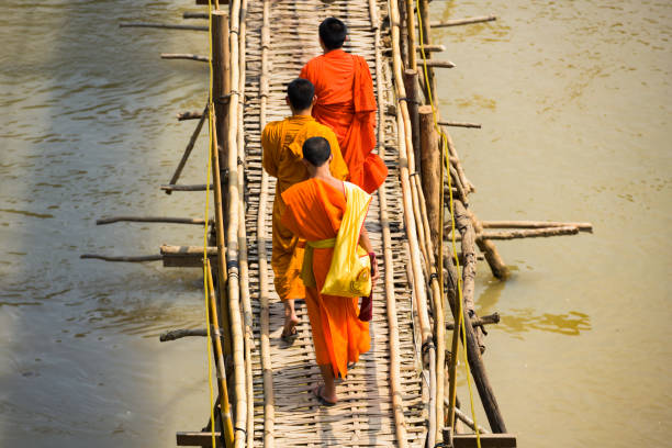 Luang Prabang, Laos - February 13, 2019. Three unidentified Buddhist monks are crossing the Bamboo Bridge that run across the Nam Khan river. The Bamboo Bridge is hand made out of bamboo and is one of the tourists attractions  in Luang Prabang, Laos.