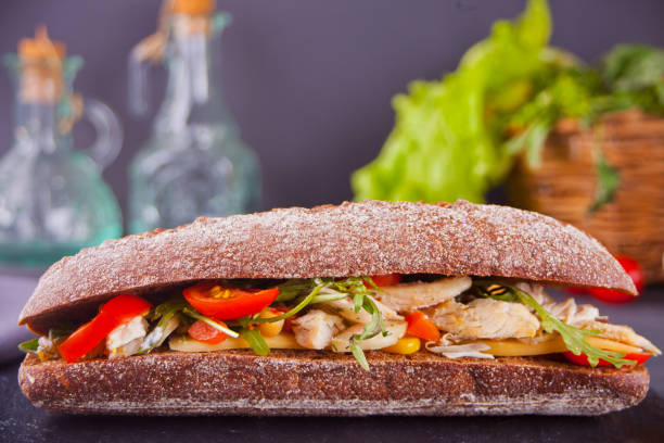 istock Baguette sandwich with turkey breast, cheese, lettuce, arugula, tomatoes and onion on a black plate. 1134842349