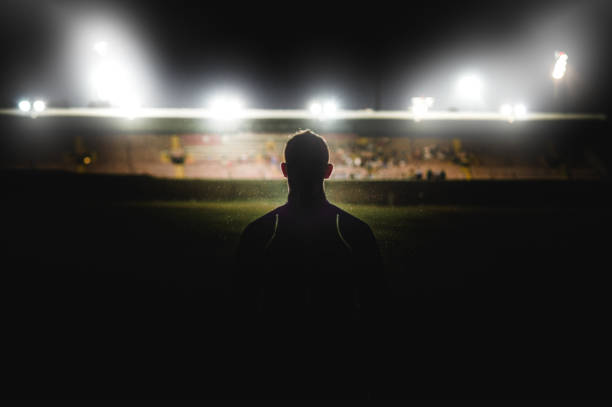 Athlete walking towards stadium silhouette A young muscular Caucasian male walking in the rain at night in front of a stadium with stadium floodlights spotlights towards the competition near Cape Town South Africa football player stock pictures, royalty-free photos & images