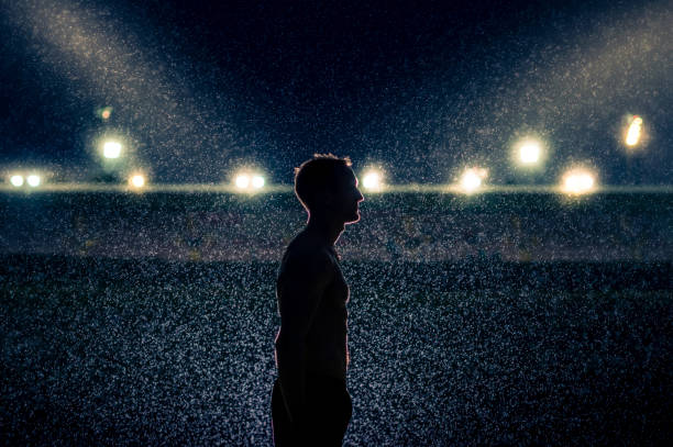 Luminous darkness Silhouette of a young muscular Caucasian male standing in the rain at night in front of a stadium with stadium floodlights spotlights near Cape Town South Africa anti doping stock pictures, royalty-free photos & images