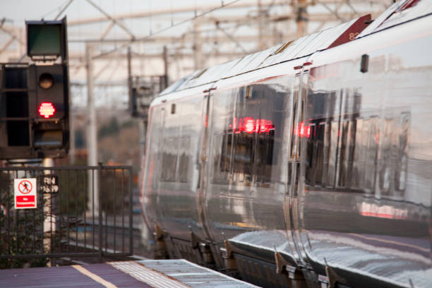 Virgin Pendolino Train and a red signal light reflected on the side of the train. The train is stopped at the platform at Rugby Station