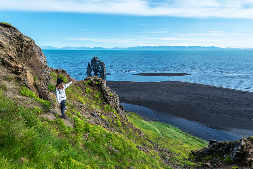 Girl tourist looking at Hvitserkur basalt stack washed with waters of Hindisvik bay in Northwest Iceland.  There is the Coastline of Arctic Ocean at Eastern shore of the Vatnsnes peninsula.