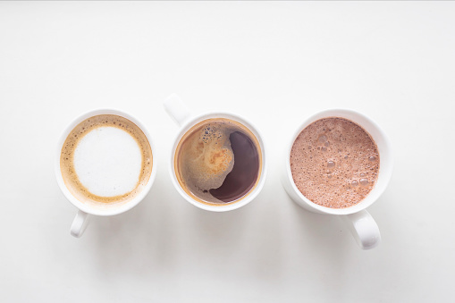 Coffee, cappuccino and cocoa in white cups on a white background. Three drinks. Top view, flat lay