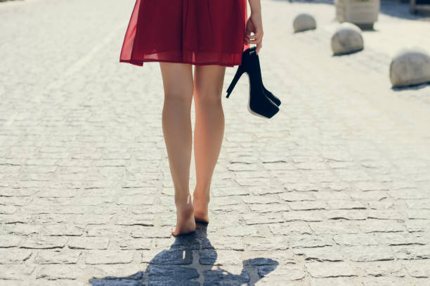 Young beautiful lady in red dress, with black high-heels in hand walking along the street barefoot; view from back, close up photo of woman's legs Young beautiful lady in red dress, with black high-heels in hand walking along the street barefoot; view from back, close up photo of woman's legs women high heels stock pictures, royalty-free photos & images
