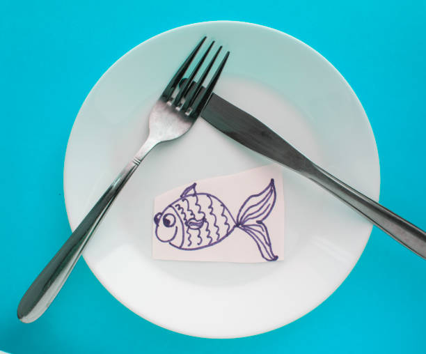 The celebration of April fool's Day, a Plate with a fork and knife and a paper fish on a blue background. Humor stock photo