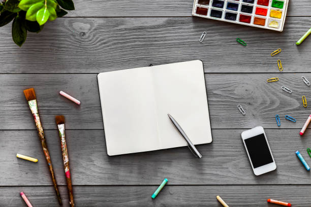 istock Colorful creative artist table with blank notebook for work sketches and paints, art paintbrushes supplies set on grey wooden background, top view, copy space, flat lay style, drawing class education 1134879632