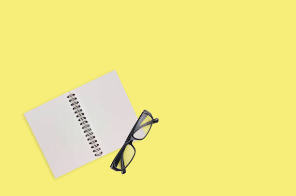 istock One transparent optical glasses in black plastic frame near paper notepad with blank sheets on table of yellow color. Top view. Business concept. Copy space for your text 1134881009