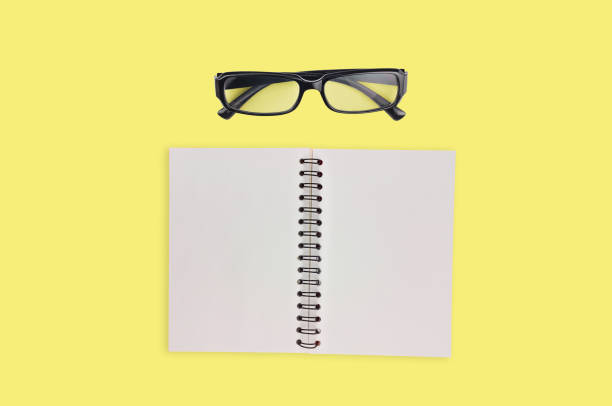 istock One transparent optical glasses in black plastic frame near paper notepad with blank sheets on table of yellow color. Top view. Business concept. Copy space for your text 1134881011