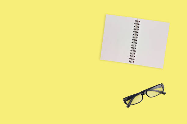 istock One transparent optical glasses in black plastic frame near paper notepad with blank sheets on table of yellow color. Top view. Business concept. Copy space for your text 1134881012