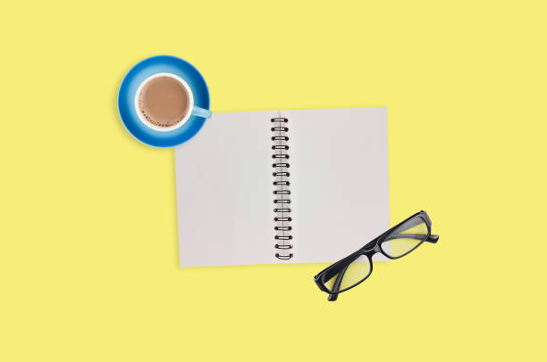 istock One transparent optical glasses in black plastic frame near paper notepad with blank sheets and full cup of coffee on table of yellow color. Top view. Business concept. Copy space for your text 1134881013