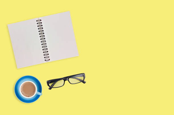 istock One transparent optical glasses in black plastic frame near paper notepad with blank sheets and full cup of coffee on table of yellow color. Top view. Business concept. Copy space for your text 1134881014