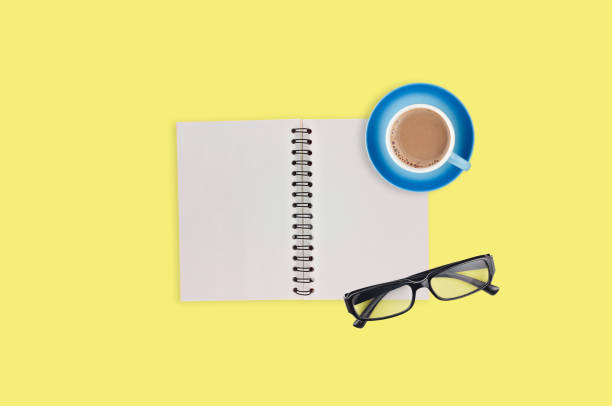 istock One transparent optical glasses in black plastic frame near paper notepad with blank sheets and full cup of coffee on table of yellow color. Top view. Business concept. Copy space for your text 1134881016