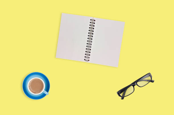 istock One transparent optical glasses in black plastic frame near paper notepad with blank sheets and full cup of coffee on table of yellow color. Top view. Business concept. Copy space for your text 1134881017