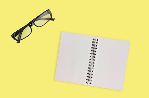 istock One transparent optical glasses in black plastic frame near paper notepad with blank sheets on table of yellow color. Top view. Business concept. Copy space for your text 1134881019
