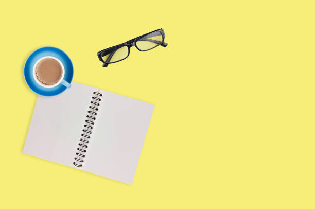 istock One transparent optical glasses in black plastic frame near paper notepad with blank sheets and full cup of coffee on table of yellow color. Top view. Business concept. Copy space for your text 1134881020