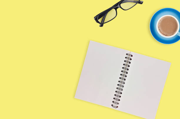 istock One transparent optical glasses in black plastic frame near paper notepad with blank sheets and full cup of coffee on table of yellow color. Top view. Business concept. Copy space for your text 1134881024